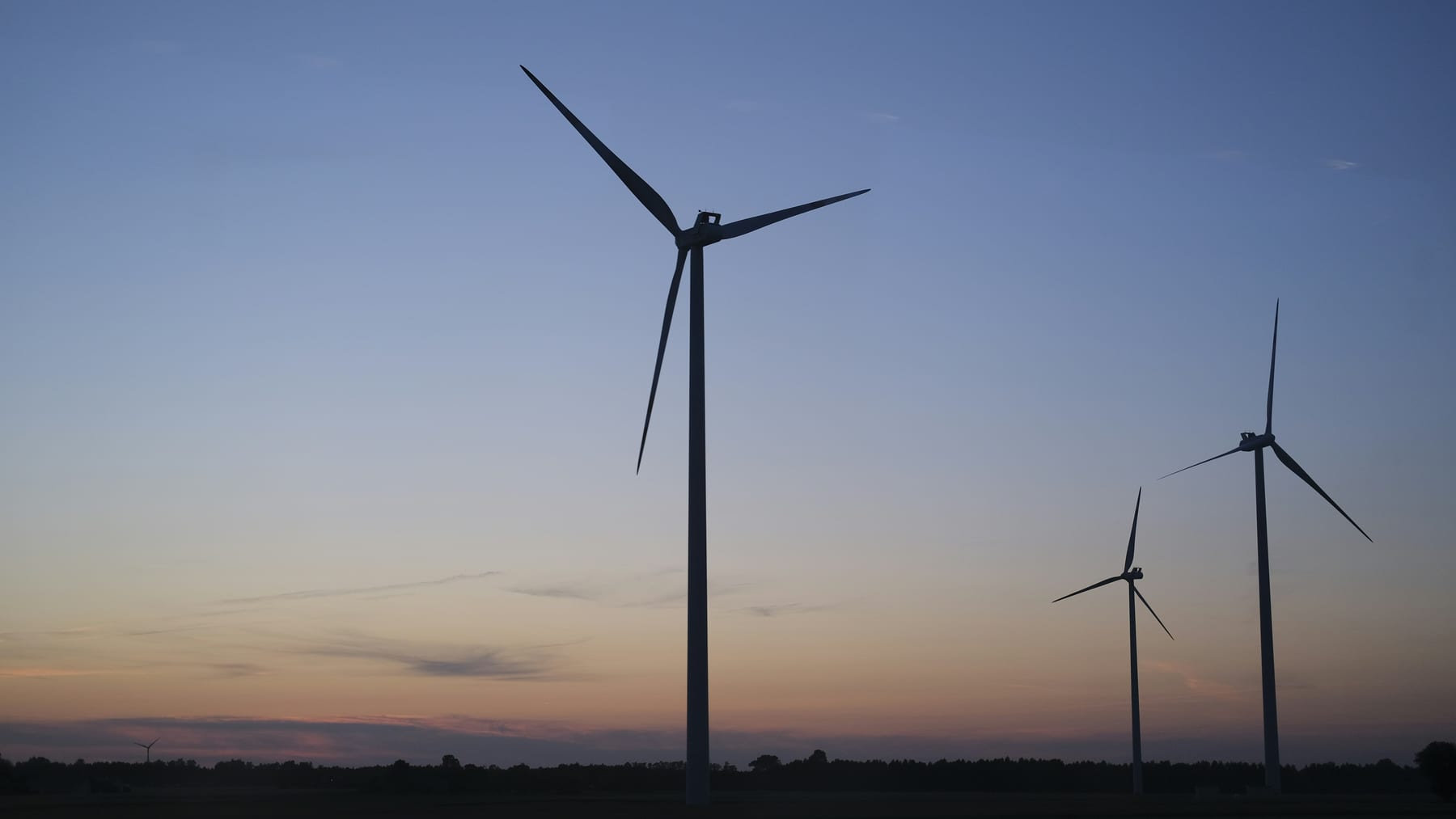 Drei Windenergieanlagen als Silhouette in der Abenddämmerung