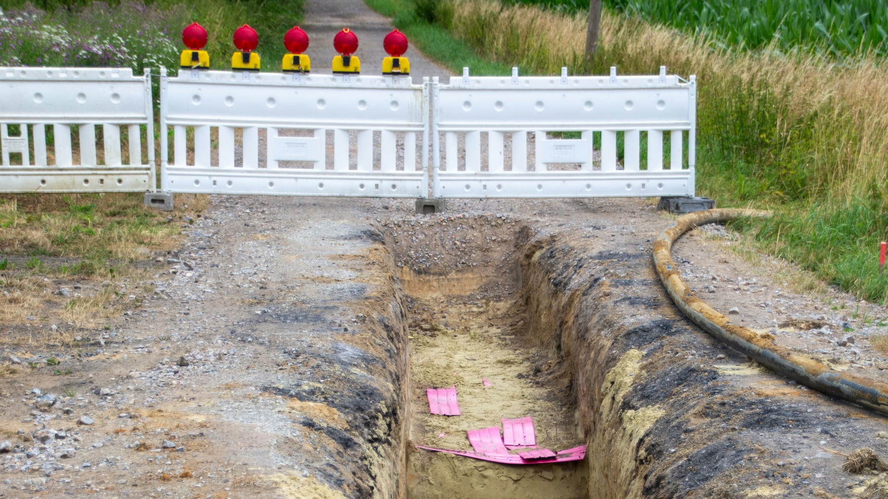 Frisch ausgehobener Kabelgraben auf einem Feldweg mit Warnband